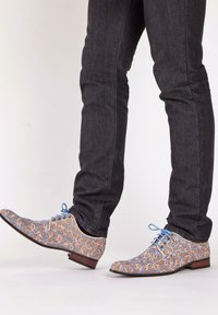 Brown and blue patterned shoes with a floral design, lace-up closure, and a low-profile heel, paired with dark jeans.