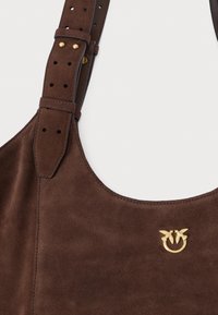 Hnedá semišová kabelka na rameno s nastaviteľným koženým remienkom, zdobená zlatým logom vtáka a hladkou textúrou.