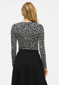 Top à manches longues noir avec un motif abstrait blanc et gris, présentant un col rond et une silhouette ajustée. Texture lisse.