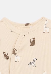 Μπεζ ριμπ ολόσωμο ρούχο με σχέδια ζώων, συμπεριλαμβανομένων γατών και ζέβρας. Διαθέτει κλείσιμο με κουμπιά και μαλακό, υφασμάτινο υλικό.