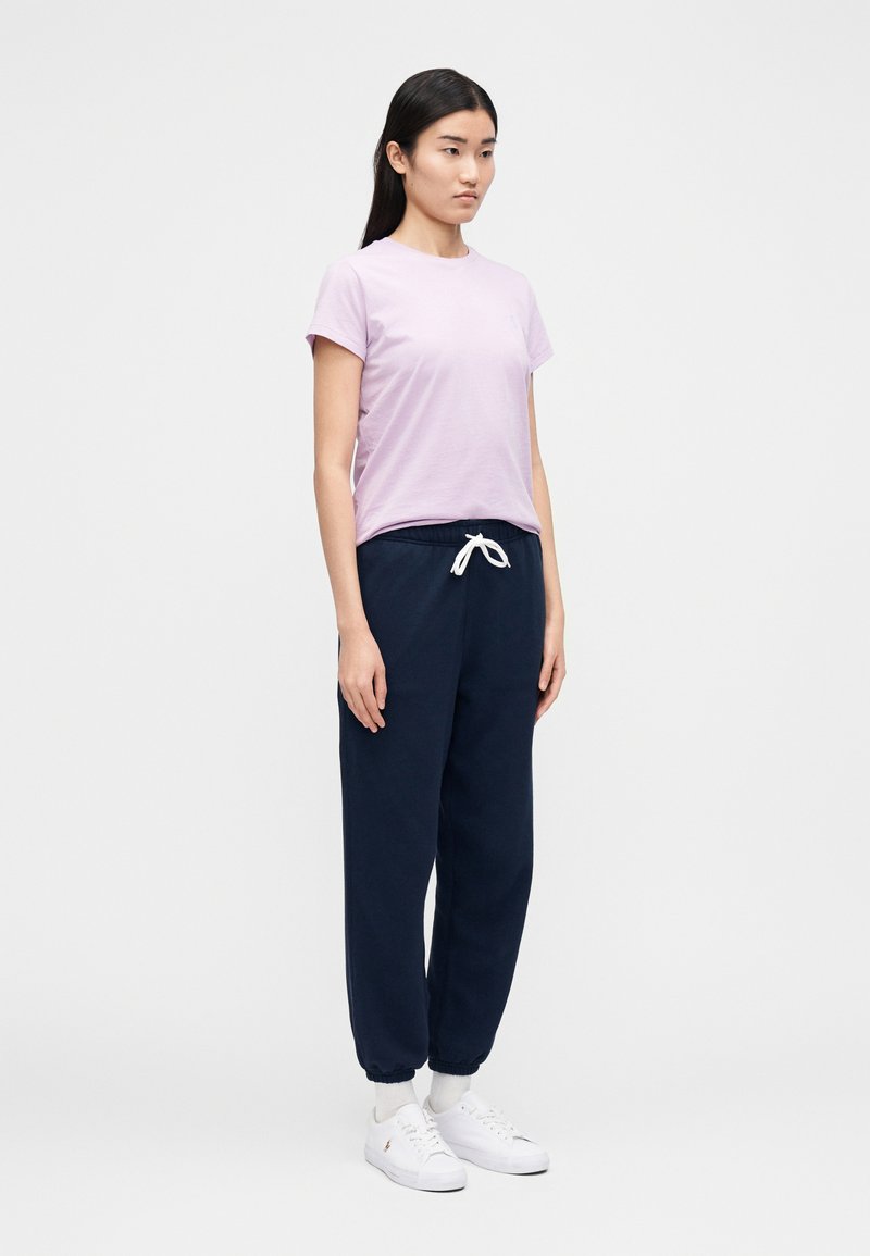 Lila t-shirt med kort ärm kombinerad med marinblå mjukisbyxor med elastisk midja och vit dragsko, kompletterade med vita sneakers.