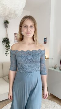 Blå spets off-shoulder topp med trekvartslånga ärmar, som har blommiga mönster; kombinerad med en lång, plisserad blå kjol. Ljus bakgrund.