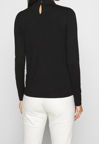 Czarna bluzka z długim rękawem, z fakturowanym kołnierzykiem i wycięciem w kształcie dziurki z tyłu, zestawiona z dopasowanymi spodniami w kolorze kremowym.