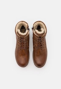 Bottes chelsea en cuir brun avec une finition texturée, intérieure doublée de fausse fourrure crème, dotées de deux crochets en métal et de lacets ronds.