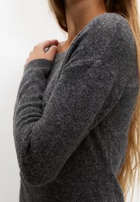 Šedý svetr s dlouhými rukávy vyrobený z texturované pleteniny, s kulatým výstřihem a přiléhavými rukávy. Měkký a ležérní design.