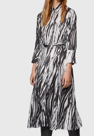 Femme portant une robe midi à manches longues à rayures zébrées noires et blanches avec un col et une ceinture assortie, debout devant un fond uni.