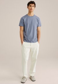 Světle modré bavlněné tričko spárované s krémově zbarvenými kalhotami. Oblečení zahrnuje šedé semišové boty a má jednoduchý, rovný design.