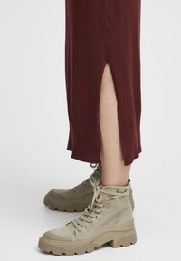 Burgundy, knälång klänning med sidoöppning; matchad med beige, högskurna stövlar med strukturerad sula och snördesign.