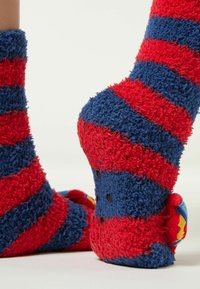 Røde og blå stribede fuzzy sokker med en blød tekstur, der har gummidutter på sålerne og livlige accenter på hælene.