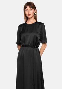 Black satin dress with short sleeves, round neckline, and a waist tie. Smooth texture and flowing silhouette, suitable for various occasions.