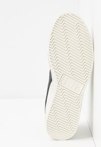 Sneaker nera con tomaia testurizzata, dotata di suola in gomma bianca e motivo a zigzag. Logo impresso sulla suola.