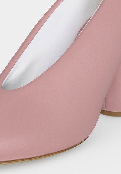 Κοντινή λήψη ροζ ψηλοτάκουνων παπουτσιών με στρογγυλεμένες μύτες και λευκή εσωτερική επένδυση σε ανοιχτό φόντο.