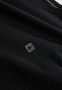 Mustmust värvi puuvillane T-särk, millel on peal vasakul küljel tekstuuriga hall rombikujuline logosilt. Sile kangas, millel on kerge sära. Klassikaline ümar kaelus.