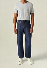 Jean en denim bleu foncé à coupe droite, avec un design classique à cinq poches et un t-shirt gris à manches courtes. Chaussures blanches à enfiler.