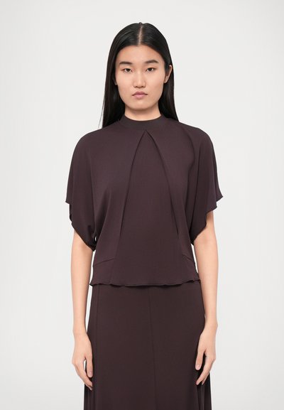 Top viola con maniche corte e larghe e un design plissettato davanti. Tessuto liscio e morbido e un collo alto completano il look.