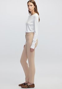 Witte lange mouwen top, aansluitende beige broek en leopardenprint flats. Glad materiaal, getailleerde pasvorm, subtiele knoopdetails op de mouwen.