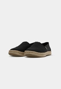 Svarta canvas espadrillor med en flätad jutesula, rund tå och subtila sömnadsdetaljer. Halvöppen design utan synliga knäppningar.