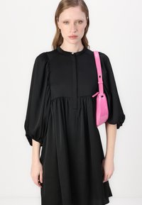 Vestido preto com cintura franzida, mangas bufantes, decote redondo e um único botão. Acompanhado por uma pequena bolsa transversal pink brilhante.