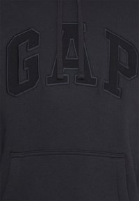 Sudadera con capucha gris oscuro hecha de algodón, con un gran logo bordado "GAP" en color a juego en la parte frontal, y un bolsillo tipo canguro en la parte delantera.
