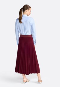 Camisa de botones azul claro y falda burdeos con pliegues y una cinturilla texturizada, combinada con zapatos de tacón beige.