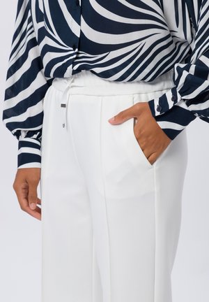 Personne portant un pantalon blanc avec la main dans la poche et une chemise à manches longues rayée zèbre bleu marine et blanc avec des poignets boutonnés.