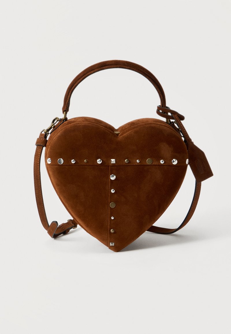 Sac à main en forme de cœur en suède marron avec des clous en métal, une poignée supérieure, une bandoulière réglable et une étiquette en cuir attachée sur un fond blanc.