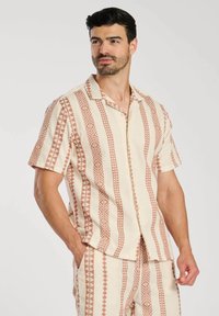 Camicia a maniche corte con base crema e motivi geometrici terracotta, dotata di chiusura con bottoni. Tessuto leggero con vestibilità comoda.