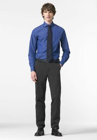 Chemise bleu à manches longues avec col boutonné, associée à un pantalon sombre et une ceinture tissée noire. La tenue comprend une cravate à pois et des chaussures noires.