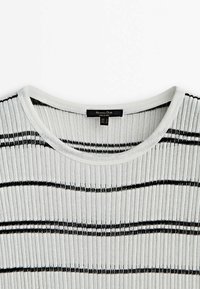 Pull en maille côtelée blanche avec des rayures noires horizontales et un col arrondi montrant une étiquette de vêtement noire.