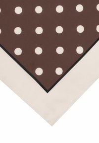 Brauner Schal mit großen weißen Punkten, an den Rändern mit einem kontrastierenden schwarzen Rand versehen, der an den Ecken in einen cremefarbenen Stoff übergeht.