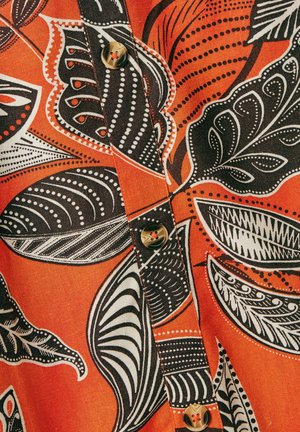 Tissu orange avec un motif de feuilles noir et blanc, avec un détail de bouton au centre. La texture est lisse et tissée.