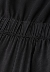 Gros plan sur un tissu noir avec une taille élastique froncée et une partie supérieure côtelée sur un vêtement.