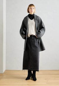 Abrigo de lana gris sobre un suéter de punto crema, falda de mezclilla negra y botines negros. El abrigo tiene grandes solapas, y la falda presenta un dobladillo deshilachado.