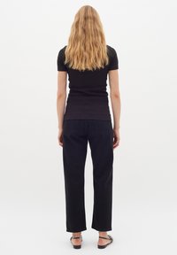 Svart åtsittande t-shirt, svarta raka jeans och svarta sandaler med remmar. Modellen står med ryggen mot kameran med vågigt axellångt hår.