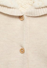Cardigan crem din tricot, cu o suprafață texturată, având un interior moale și pufos și două butoane rotunde din lemn în față.