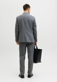 Szary wełniany garnitur z dopasowaną marynarką i spodniami, z fakturowanej tkaniny, zestawiony z czarną torbą typu tote i czarnymi butami.