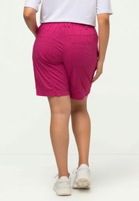 Fuchsia shorts met een elastische tailleband, voorzien van twee achterzakken en een zachte textuur. Gepaard met witte sneakers.