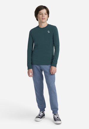 Long-sleeve teal shirt with small white logo, paired with light blue joggers and black sneakers with white laces. Simple design and fit.