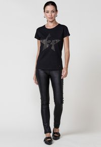 Zwarte t-shirt met een glanzend, textuur ontwerp van een ster, gecombineerd met slim-fit zwarte neplederen broek met een krokodillenstructuur.