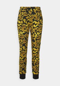 Svarta träningsbyxor med ett snurrande guldmönster, tillverkade av mjukt material, med elastisk midja och mudd.