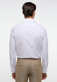 Witte lange mouwen shirt met een gladde textuur en knoopmanchetten, gecombineerd met tan linnen broek met achterzakken en decoratieve knopen.