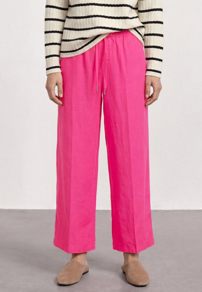 Personne portant un pantalon large rose vif, des chaussures beiges sans lacets et un pull blanc à rayures horizontales noires.
