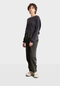 Dunkelgrauer gerippter Pullover, lässige dunkelgraue Denim-Jeans und hellbeige Sneaker. Zu den bemerkenswerten Details zählen umgeschlagene Ärmel und eine entspannte Passform.