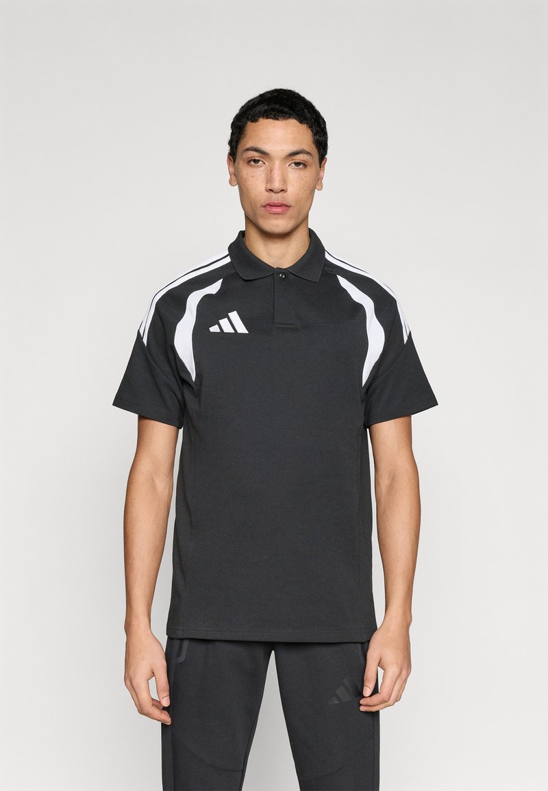 Μαύρο πόλο πουκάμισο με λευκές λεπτομέρειες, κοντά μανίκια και γιακά. Διαθέτει το λογότυπο της Adidas στο αριστερό στήθος και ριγέ μοτίβο στους ώμους.