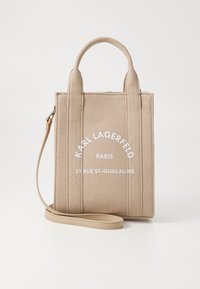 Beige kanvas håndveske med to korte håndtak og en avtakbar stropp. Har hvittrykt tekst på forsiden og en strukturert rektangulær form.