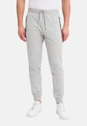 Grå bomullsbyxor med elastisk midja och dragsko. Har sidofickor med dragkedja och ribbade mudd. Kombination med vita sneakers.