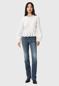Witte blouse met lange mouwen, met geplooide textuur en een gerimpelde zoom, gecombineerd met blauwe spijkerbroek en zwarte puntige enkellaarzen.
