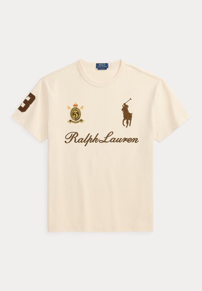 Μπεζ T-shirt Ralph Lauren με καφέ λογότυπο παίκτη πόλο, αριθμό 3 στο δεξί μανίκι και έμβλημα με θυρεό στο αριστερό στήθος.