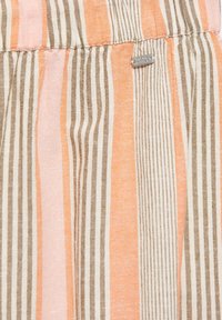 Tissu rayé vertical en rose, orange, beige et blanc avec une petite étiquette métallique indiquant "Pacific Republic" cousue près de la couture supérieure.
