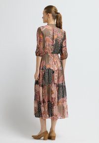 Dlouhé šaty s vzorem a nabíranými rukávy v odstínech růžové, černé a krémové; vrstvený design a stažený pas; nošeny s béžovými podpatky.